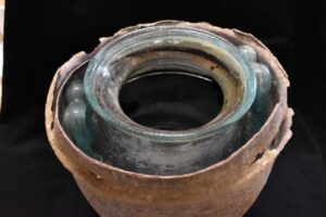 a glass bottle inside a leaden pot, containing dark-colored liquid