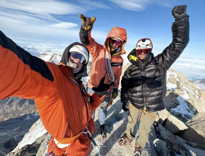 Three young climbers smile and cheer from the summit of Fitz Roy. 