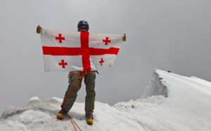 A climber holds a Georgian flag on the summit of a 7,000'er in the Hindu Kush.
