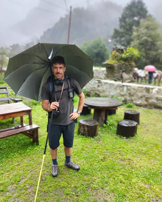 Helias Millerioux in a green mountain setting, with an umbrella under the rain.