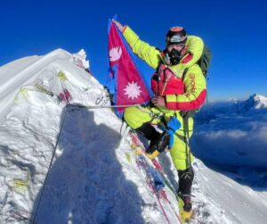 A climber on O2 holds a Nepalese flag on a spiky summit.