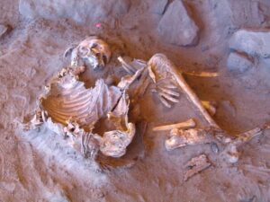 A skeleton curled up, half buried in dry earth.